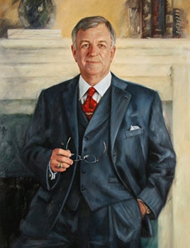 commissioned portrait of a middle-aged man posing with his glasses off and in hand, wearing a suit and tie in front of a mantelpiece.